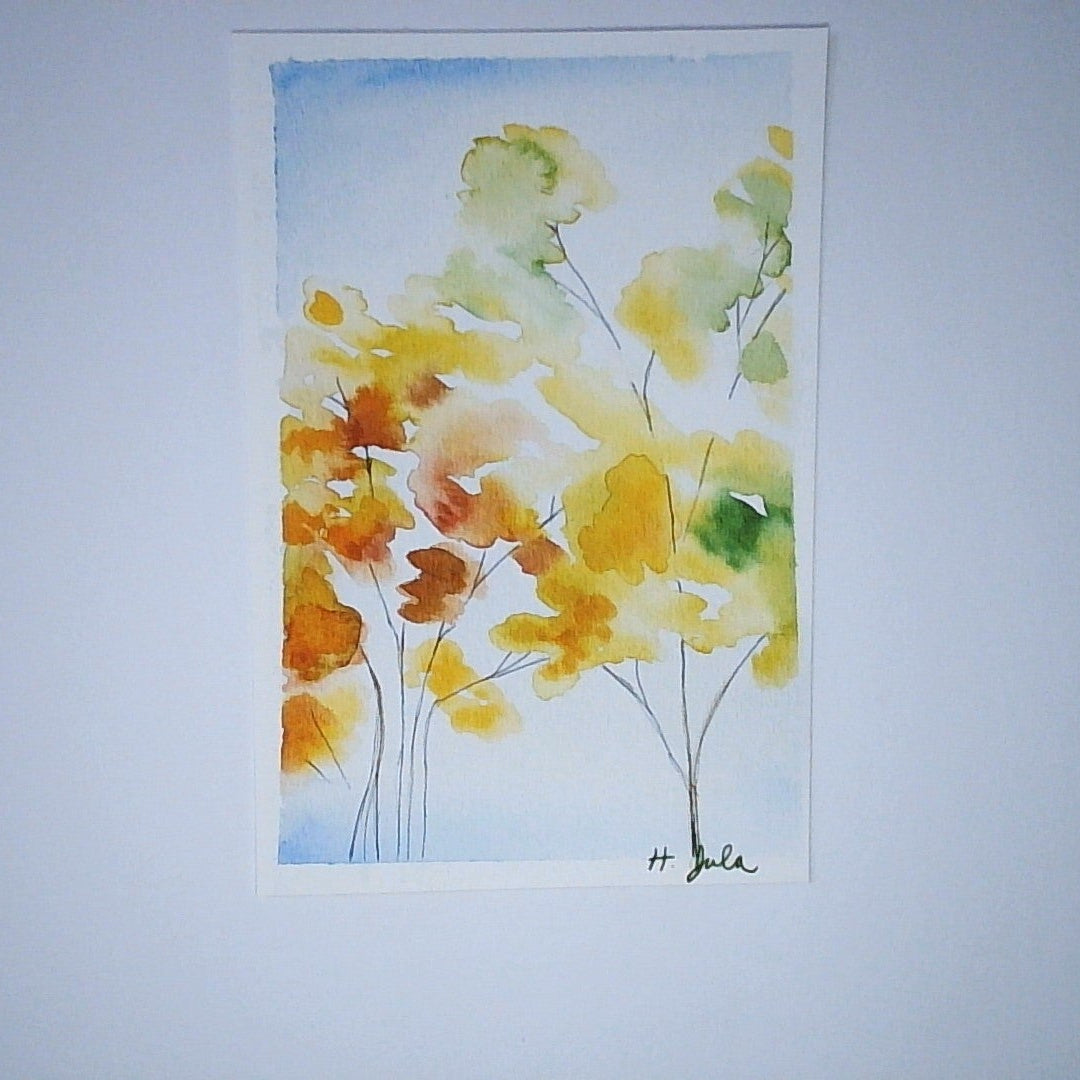 A vertical watercolor painting of yellow and orange trees on a light blue background, mounted on a white wall.